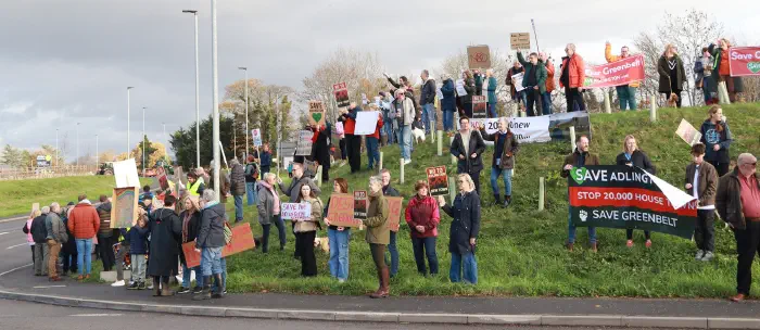 Wide shot of the hillside by roundabout full of a crowd all holding banners and placards