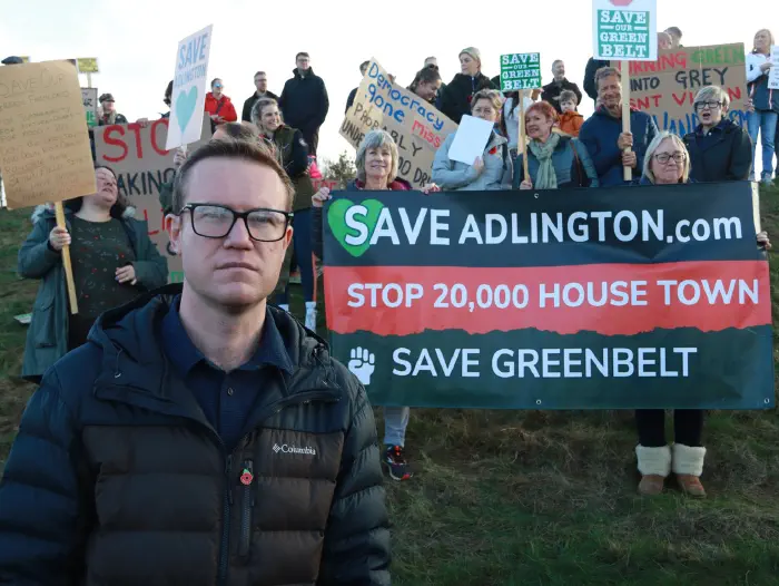 Tim Roca MP standing infront of a Save Adlington banner and crowd holding placards