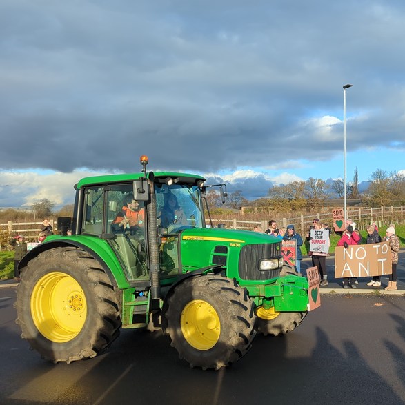 Green John Deere Tractor on the roundabout with Save Adlington placard on front surrounded by protesters